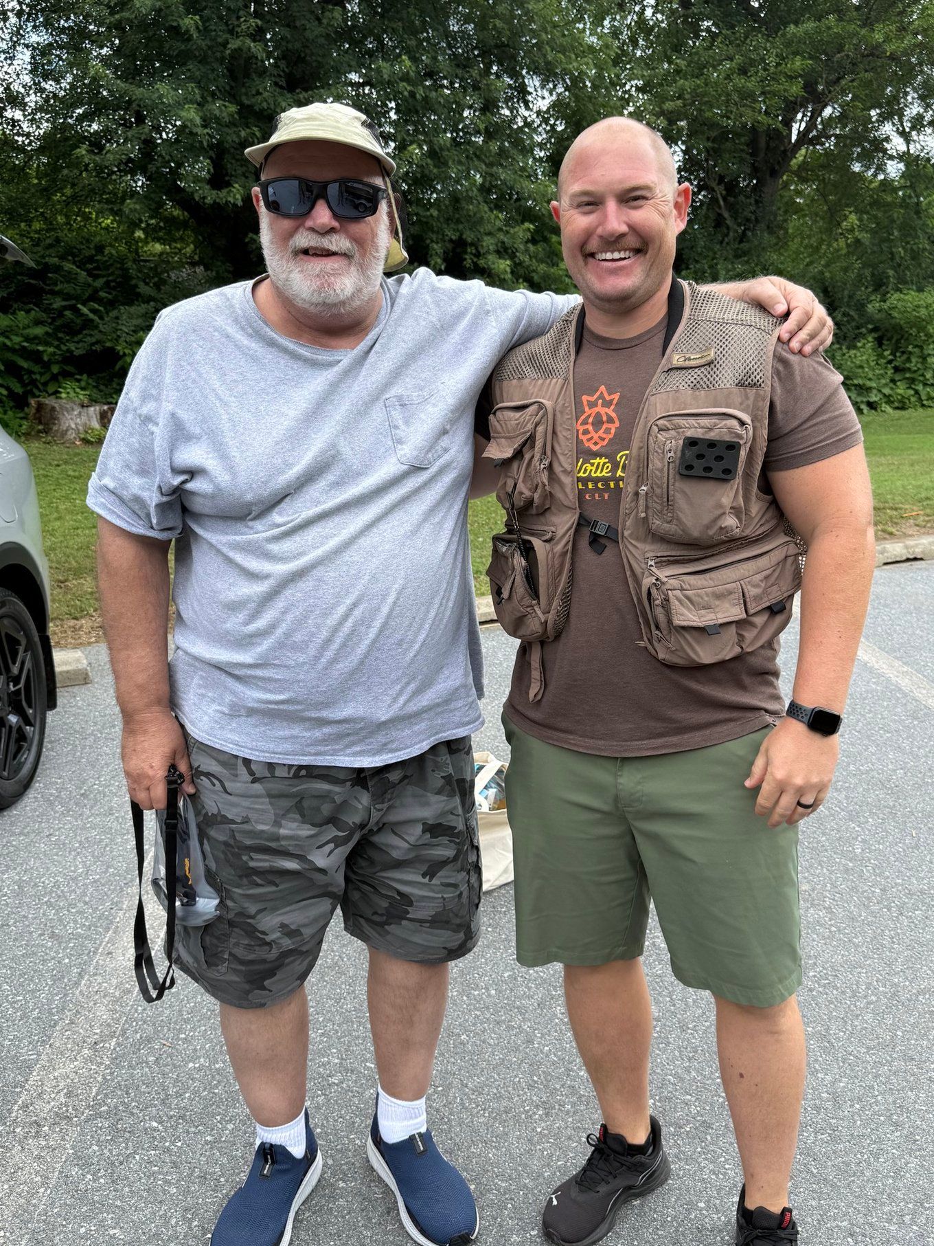Two outdoor enthusiasts standing together on pavement with trees in background