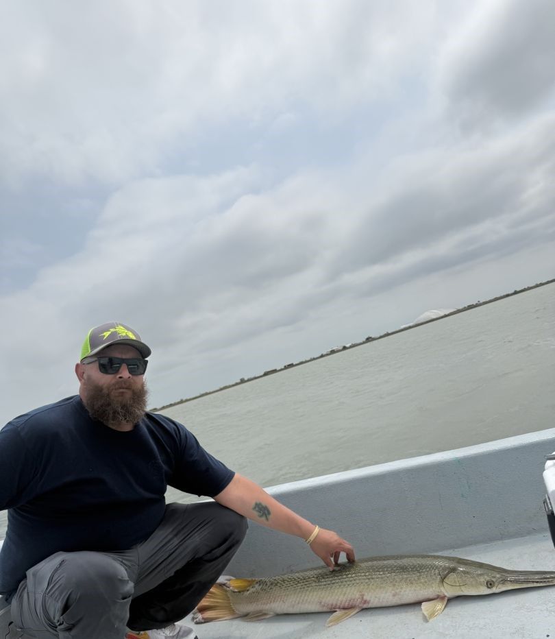 Angler displaying caught alligator gar on boat deck