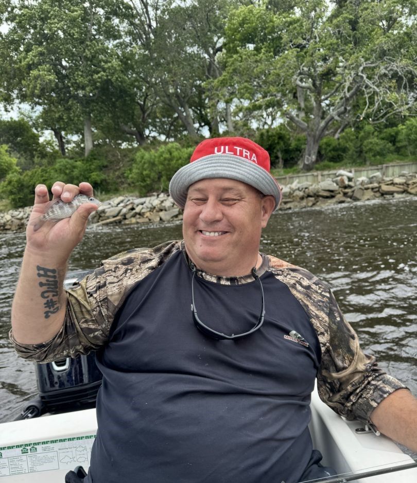 Angler holding small fish in boat on calm water with trees in background