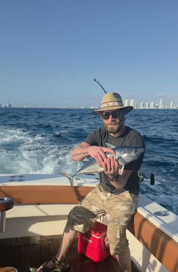 Angler holding freshly caught fish on boat deck with ocean and city skyline in background