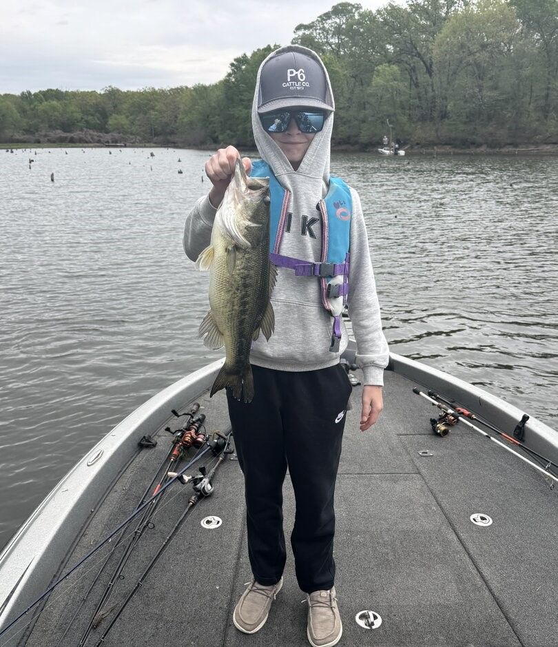 Bass fish held up on fishing boat with multiple fishing rods visible on deck