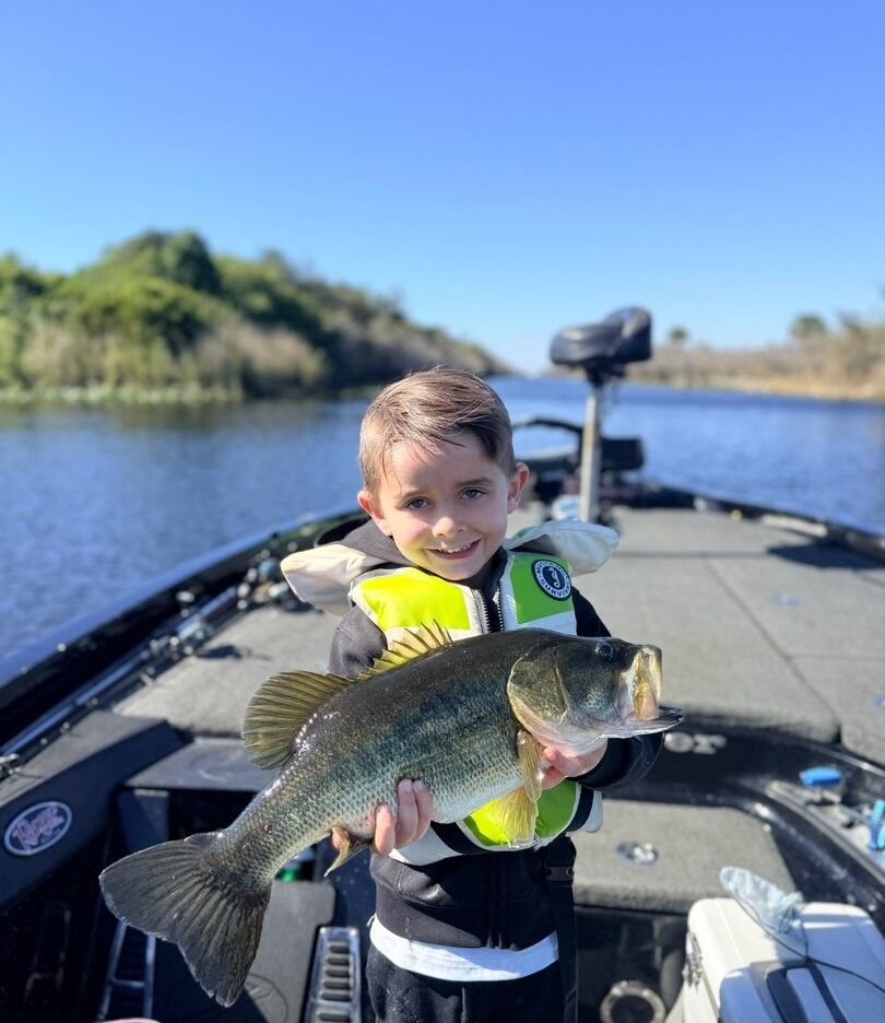 Large bass fish being held on fishing boat with water and vegetation in background