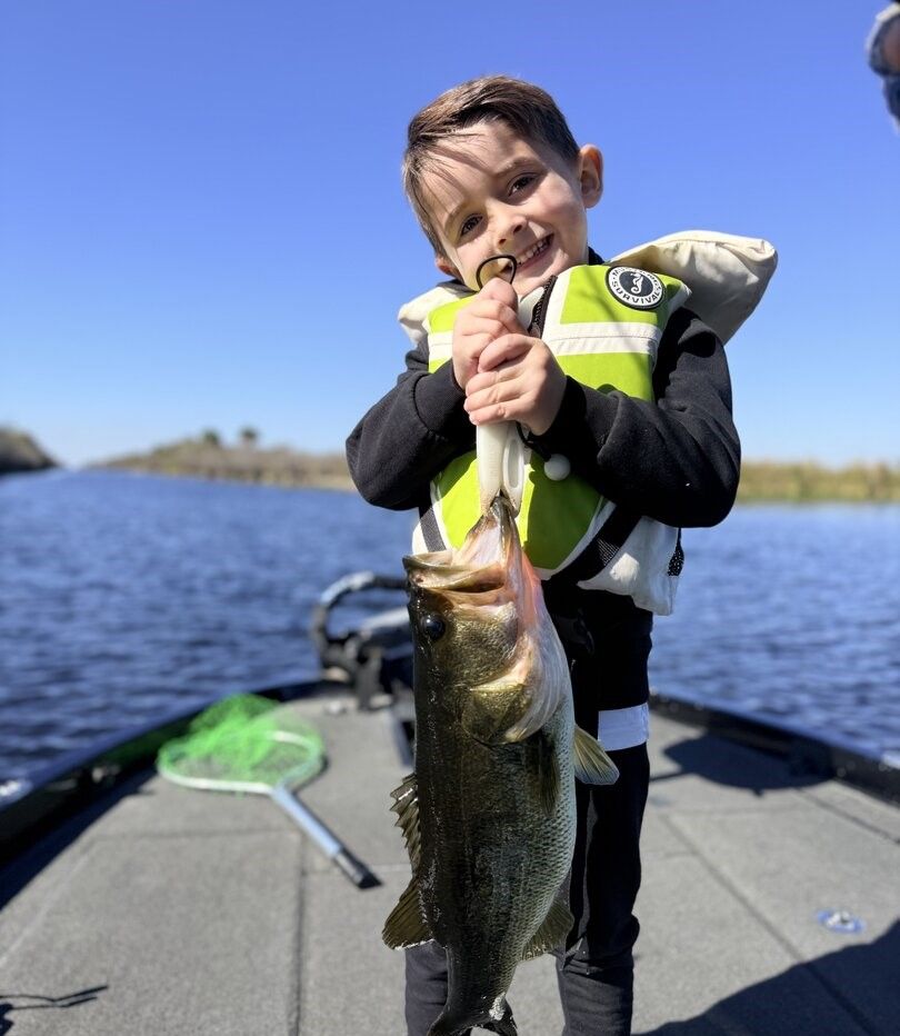 Large bass fish being held up on fishing boat deck with net visible