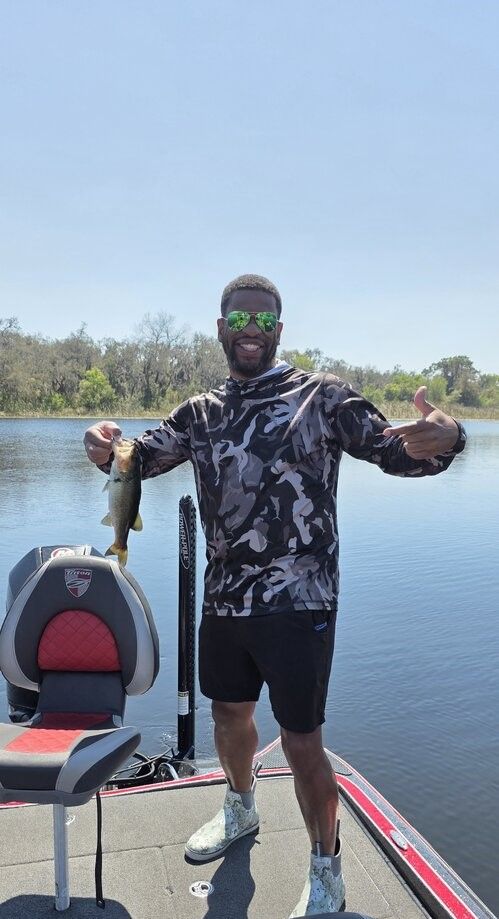 Angler holding caught bass fish on fishing boat in calm lake water