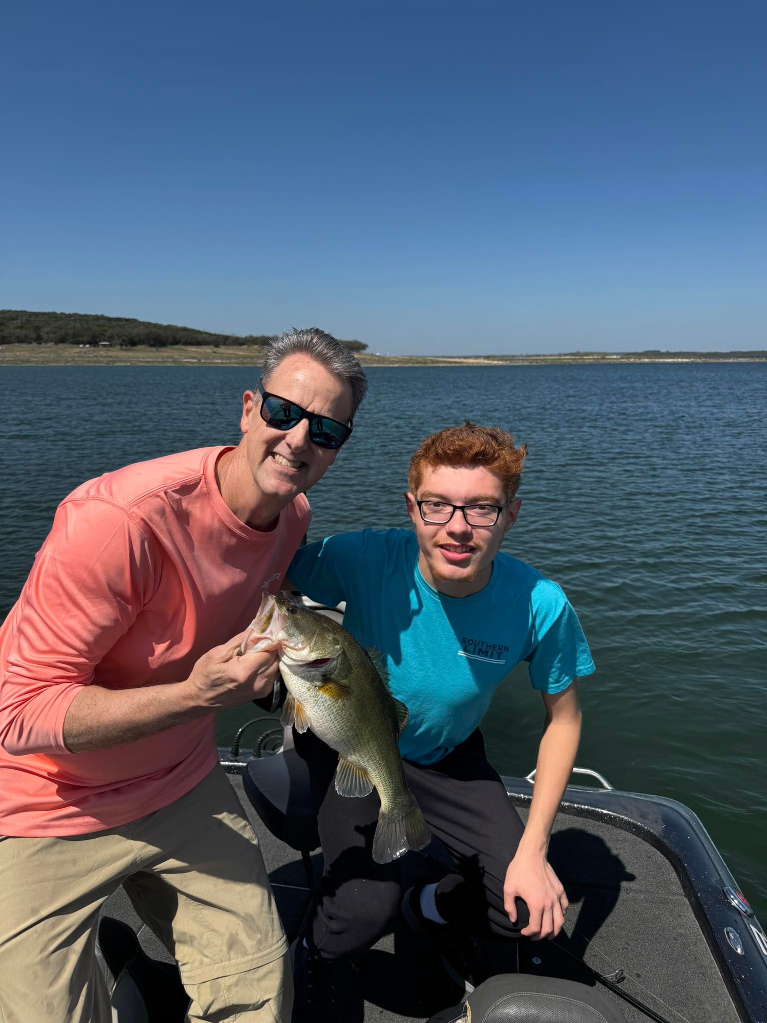 Two people on a boat holding a freshly caught bass on a lake