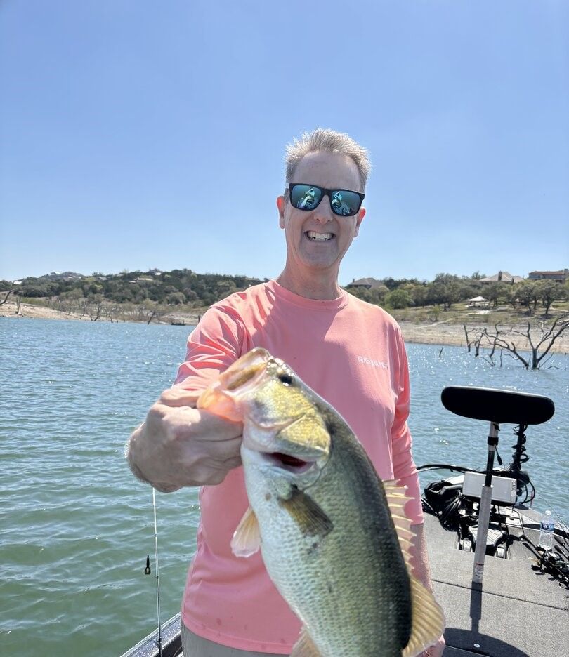 Angler holding large bass fish on boat at lake