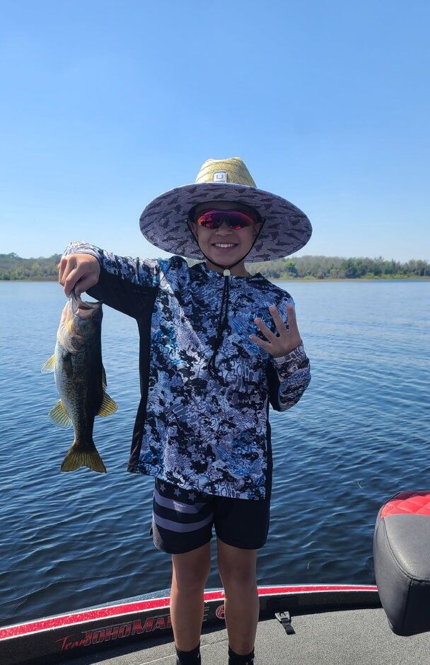 Angler holding caught bass fish on boat deck over lake water