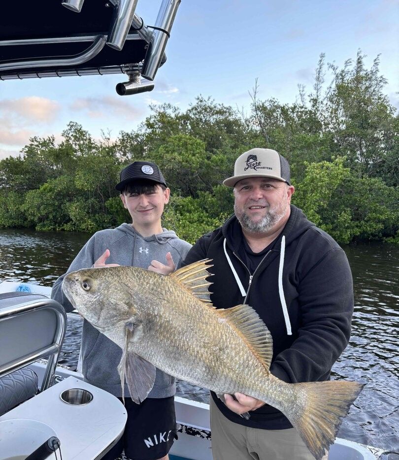 Black drum fish catch displayed on fishing boat with trees in background