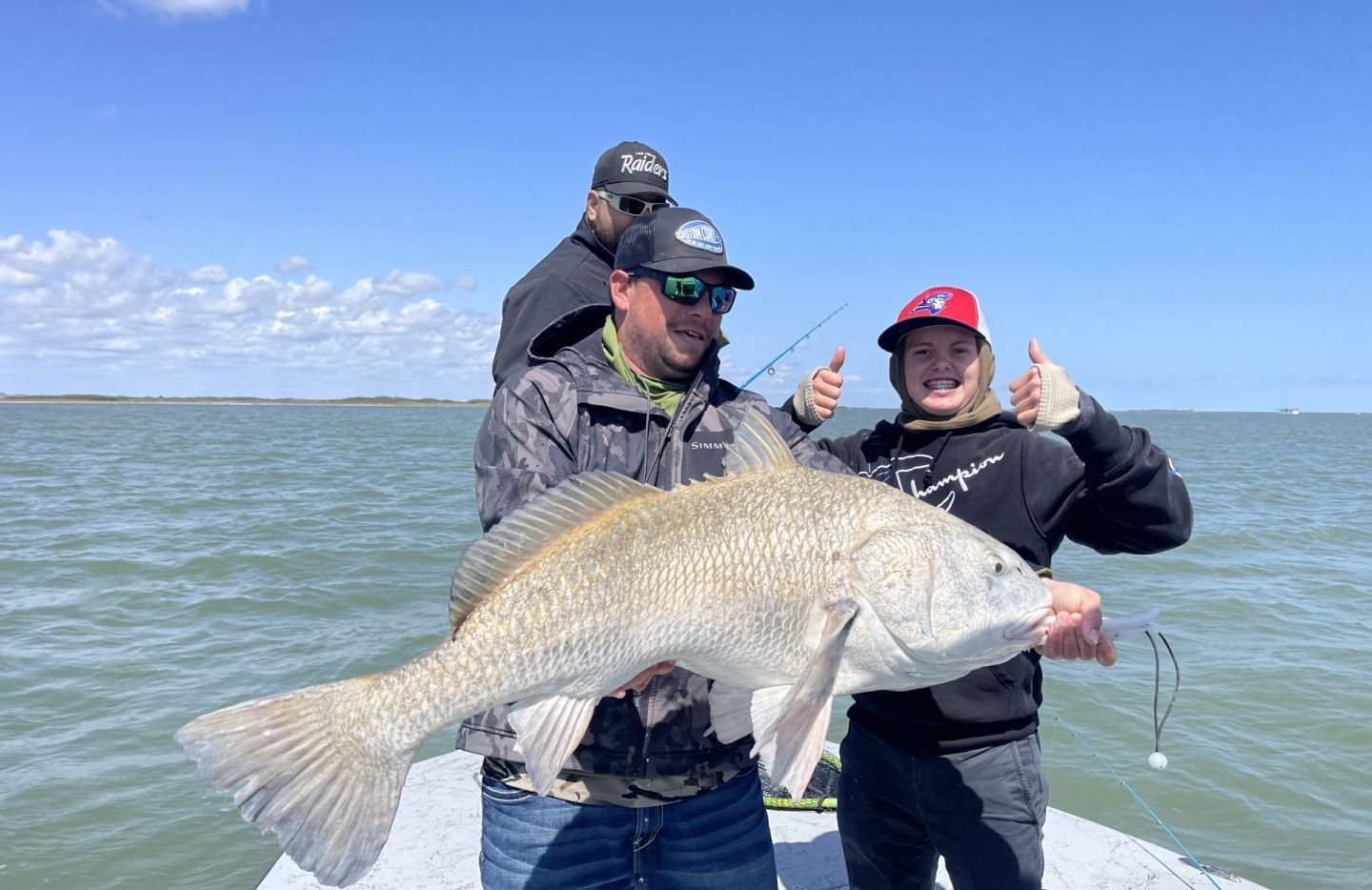 Large black drum fish being held on fishing boat with blue sky and water in background