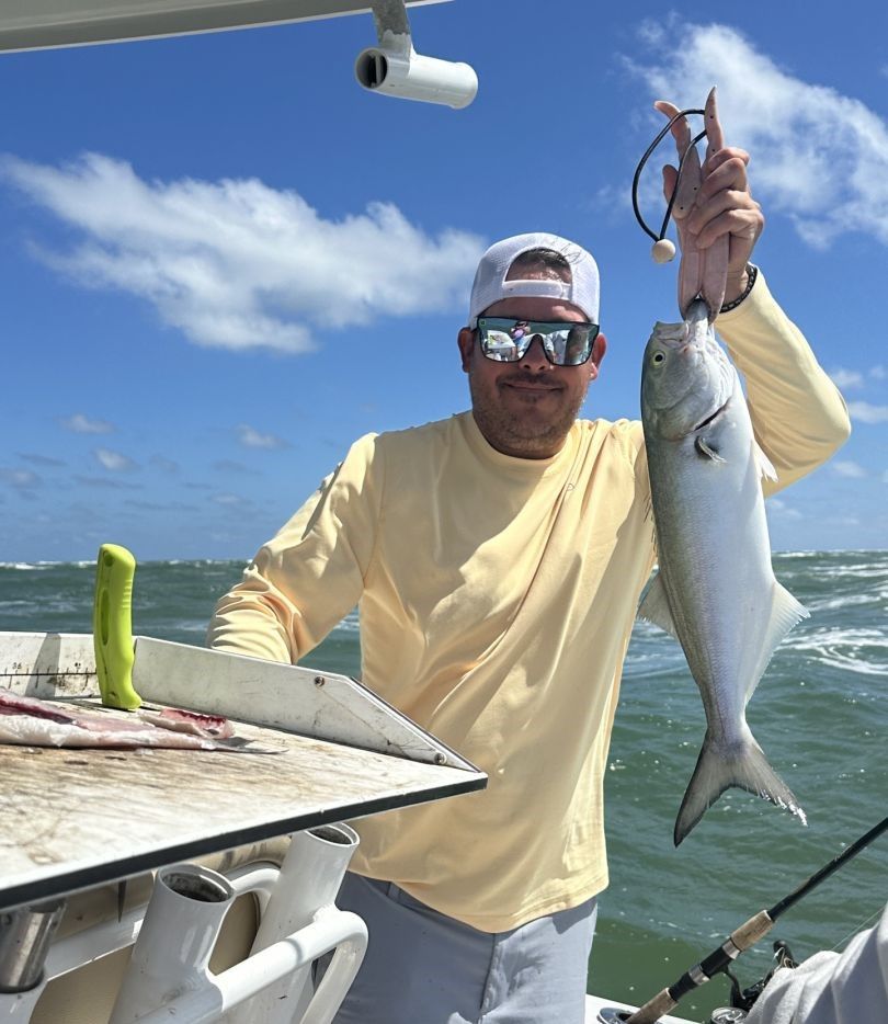 Angler holding freshly caught bluefish on fishing boat deck over ocean water