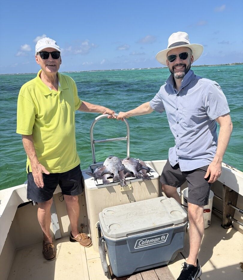 Two people on a boat displaying their catch of fish on deck with ocean water in background
