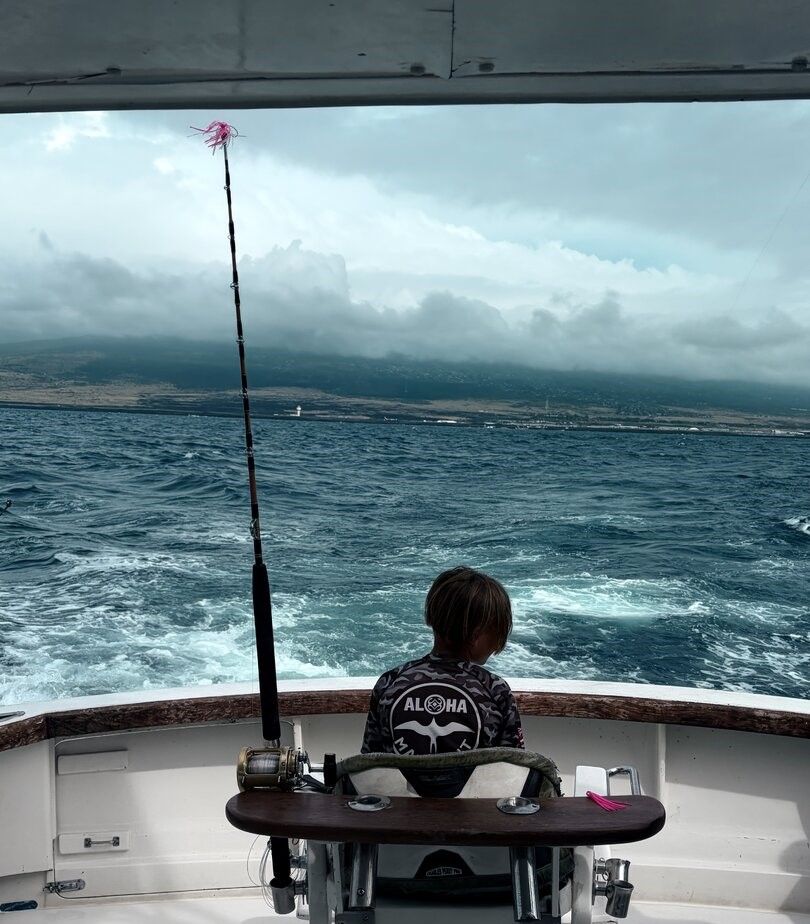 Fishing rod setup on boat stern with ocean wake and mountainous coastline in background