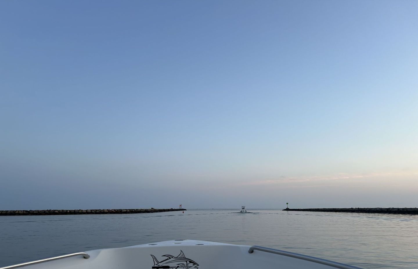 Boat bow on calm water approaching harbor entrance with breakwaters and lighthouse structures