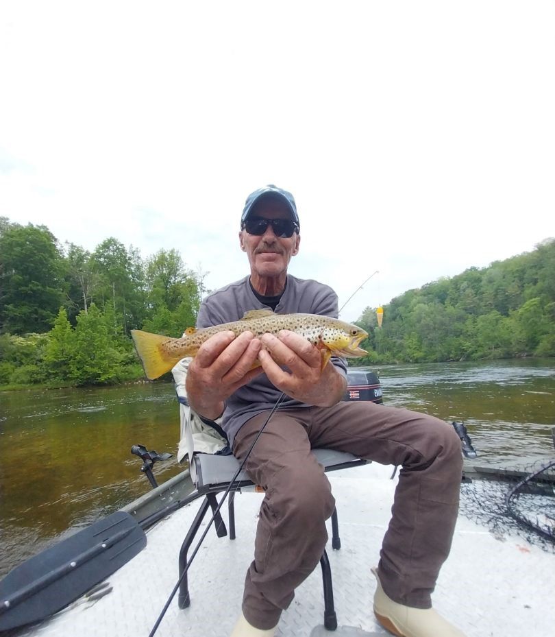 Brown trout caught while fishing from boat on river surrounded by green trees