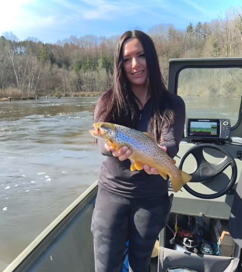 Brown trout catch displayed on fishing boat with river and forested hills in background