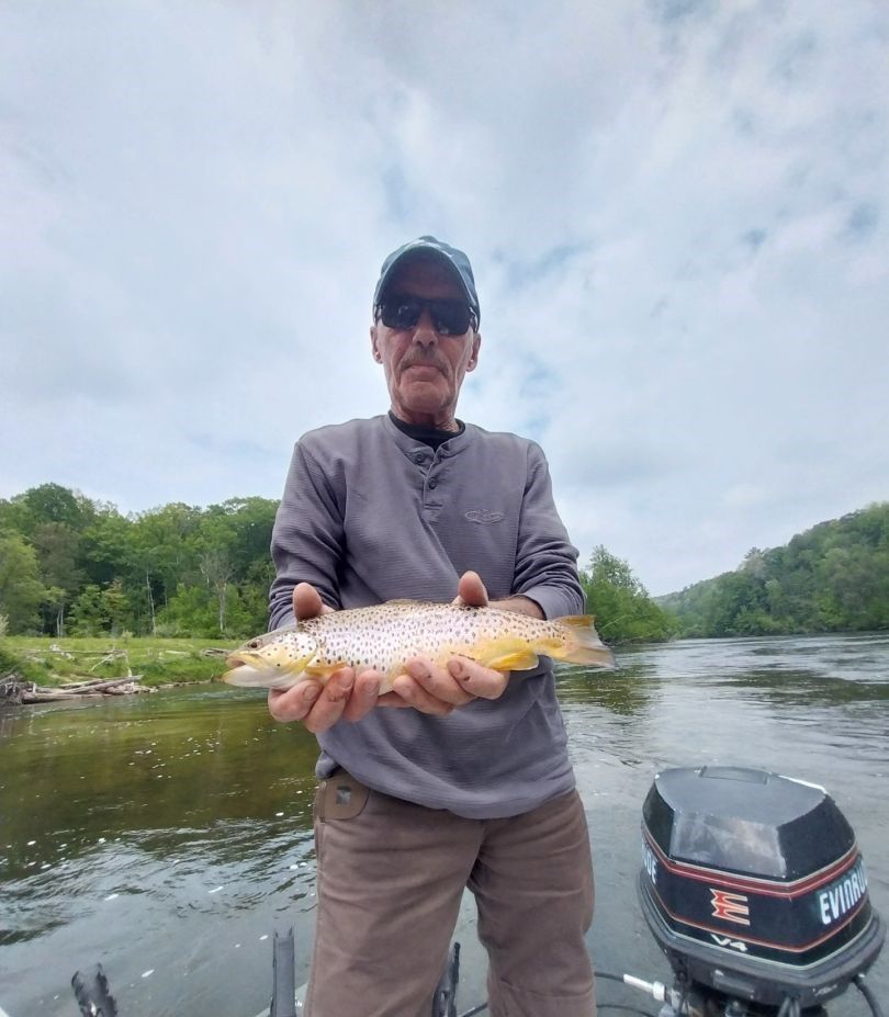 Angler holding caught brown trout on river with boat and forested shoreline