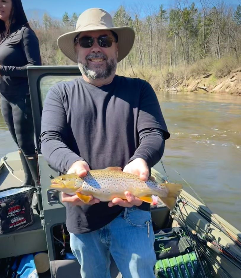 Brown trout held on fishing boat with river and forest backdrop