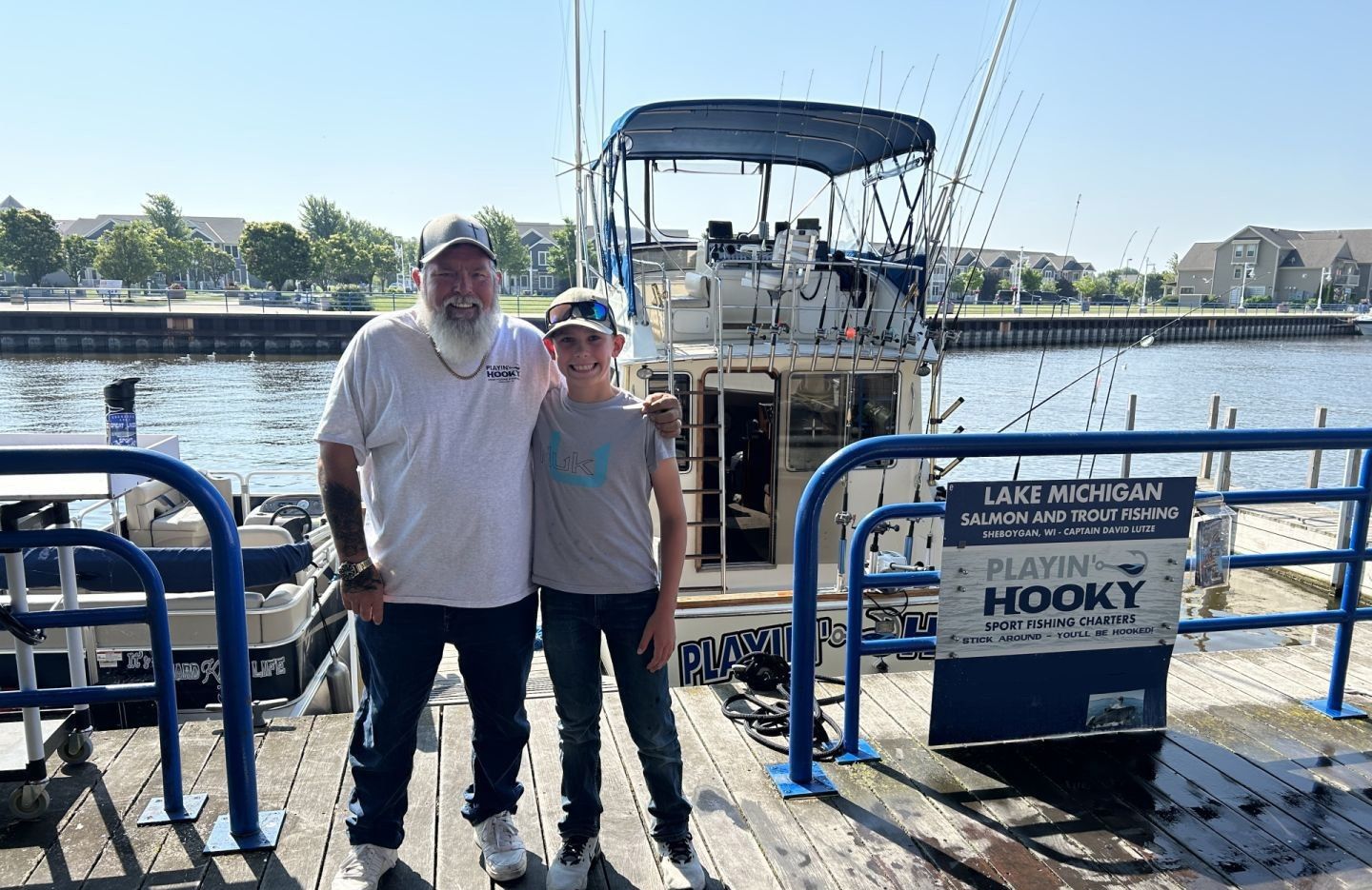 Two people standing on dock next to charter fishing boat with Lake Michigan salmon and trout fishing signage