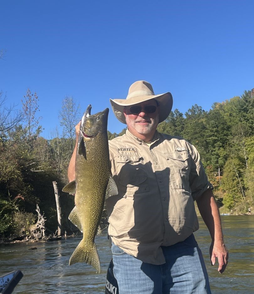 Angler holding freshly caught Chinook salmon by river with trees in background