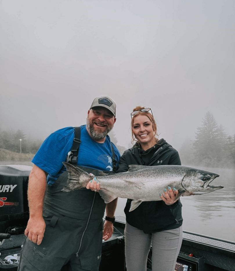 Two people holding a large Chinook salmon on a fishing boat in foggy conditions