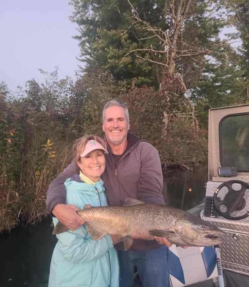 Two people holding a large Chinook salmon outdoors near a boat