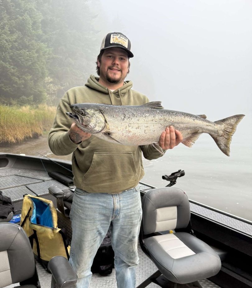 Angler holding large Chinook salmon on fishing boat in misty outdoor setting