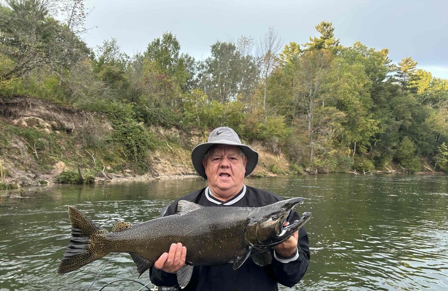 Angler holding large Chinook salmon on river with forested shoreline