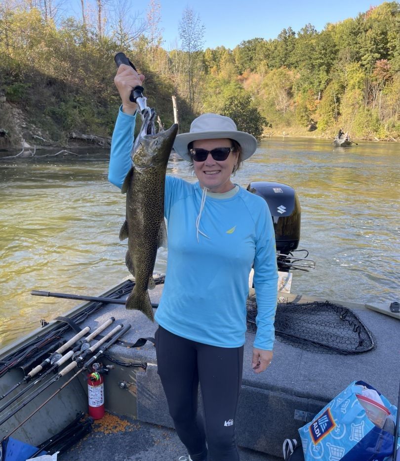 Angler holding caught Coho Salmon on fishing boat with rods and net visible