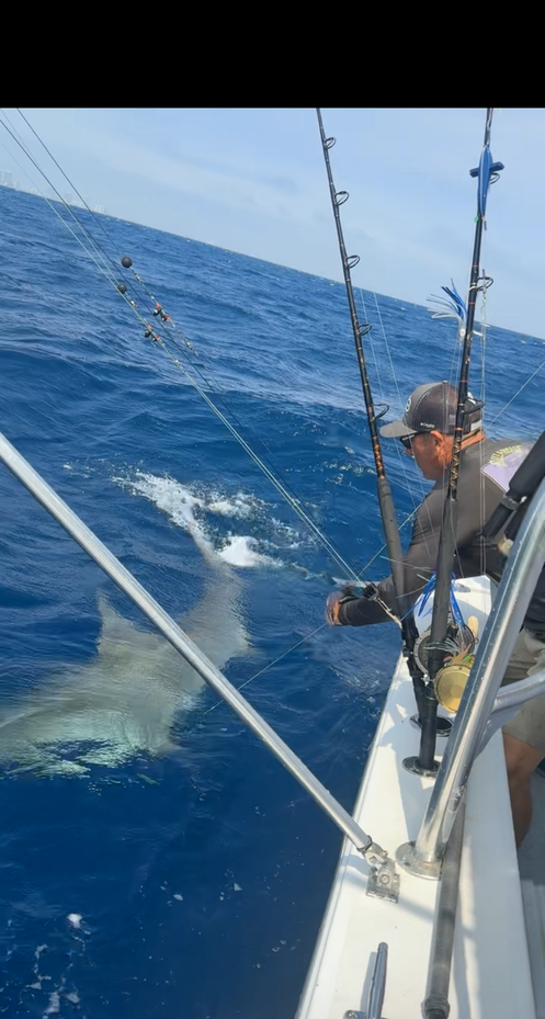 Deep sea fishing action with large fish creating splash in blue ocean water near fishing boat