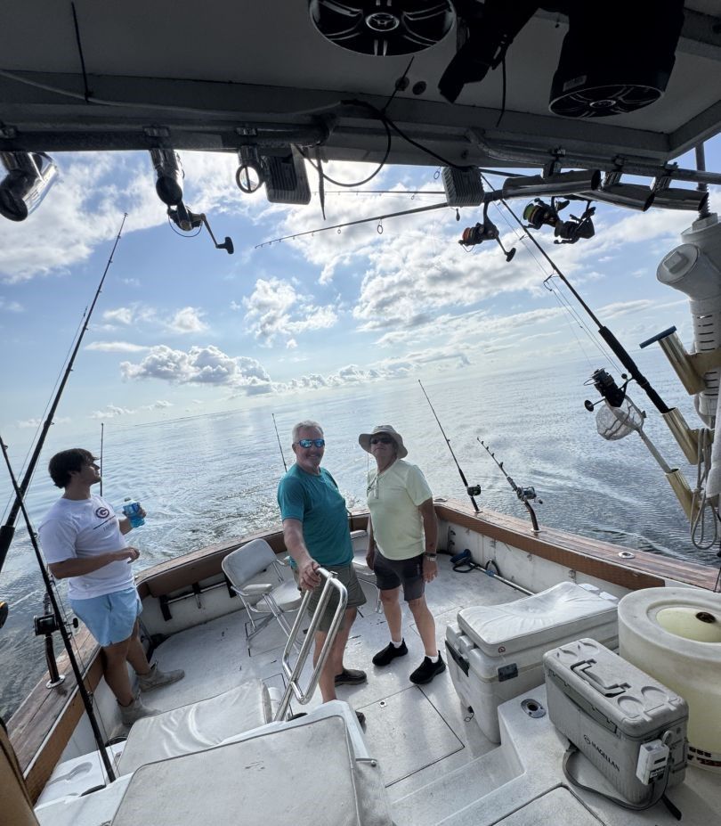 Fishing boat deck with multiple fishing rods set up over open ocean water under cloudy sky