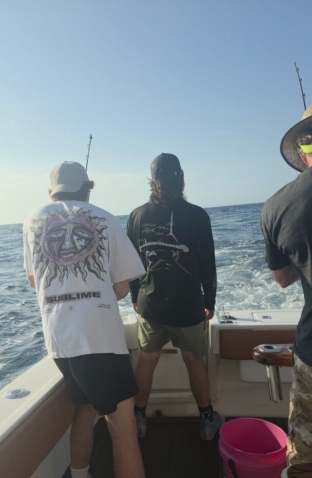 Fishing boat on open ocean water with fishing rods and equipment visible on deck