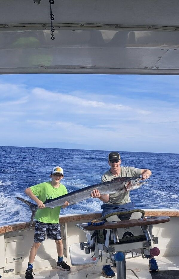 Two people holding a large fish on a fishing boat at sea