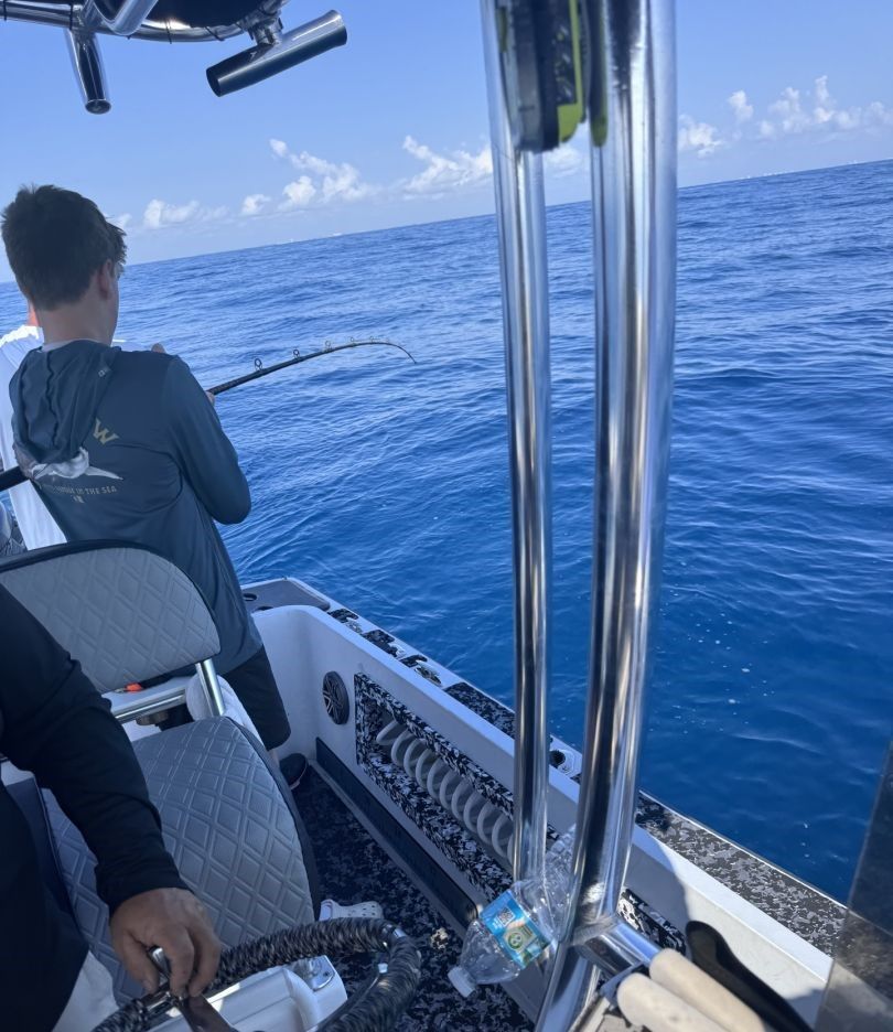 Deep sea fishing rod bent with tension over blue ocean waters from fishing boat deck