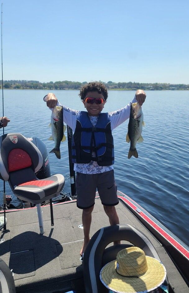 Two freshly caught bass displayed on fishing boat deck on calm lake water