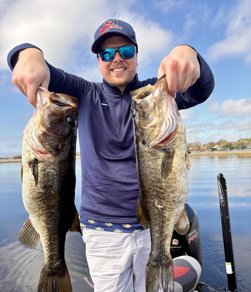 Two large bass being held up after successful fishing trip on calm water