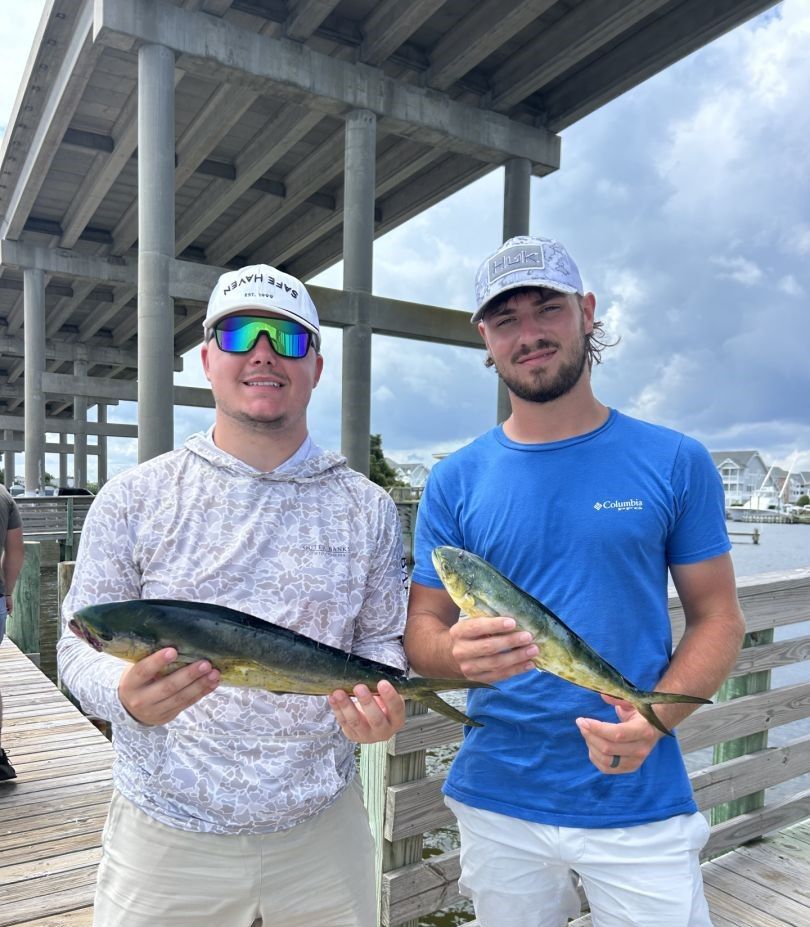 Two anglers displaying freshly caught mahi mahi fish on wooden dock under bridge