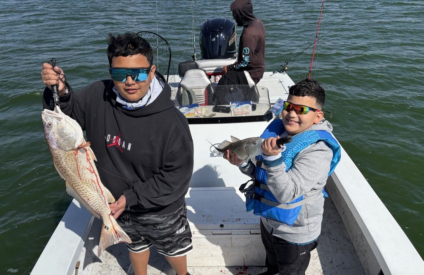 Two anglers displaying freshly caught redfish on fishing boat