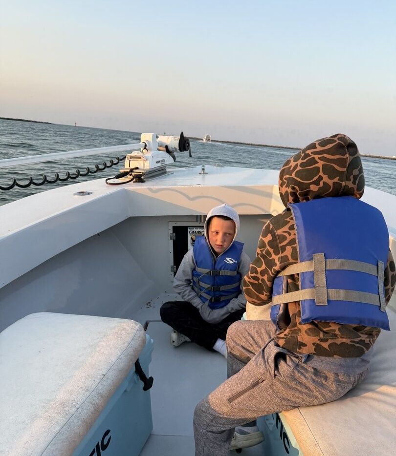 Two people on a fishing boat deck wearing life jackets during evening boating trip