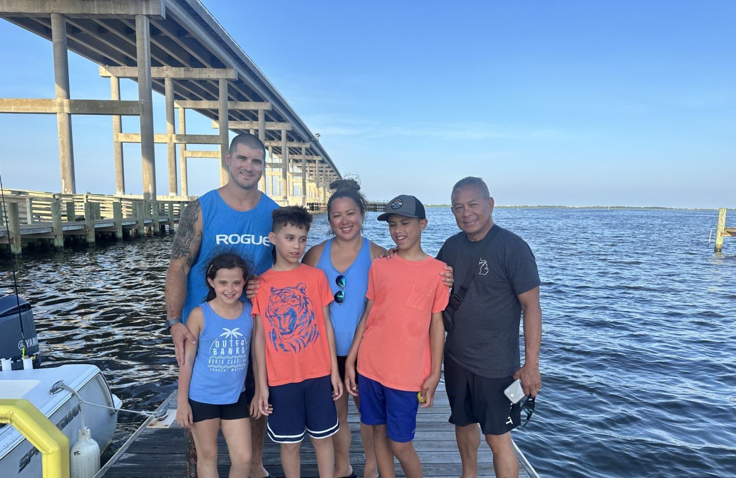Family group standing on wooden dock with bridge and water in background
