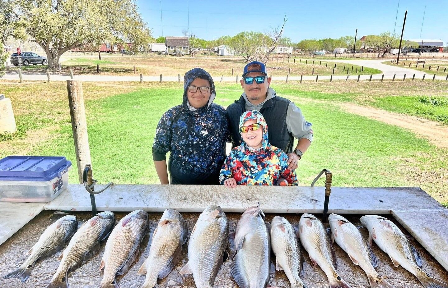 Family fishing trip displaying ten redfish catch laid out on cleaning table outdoors