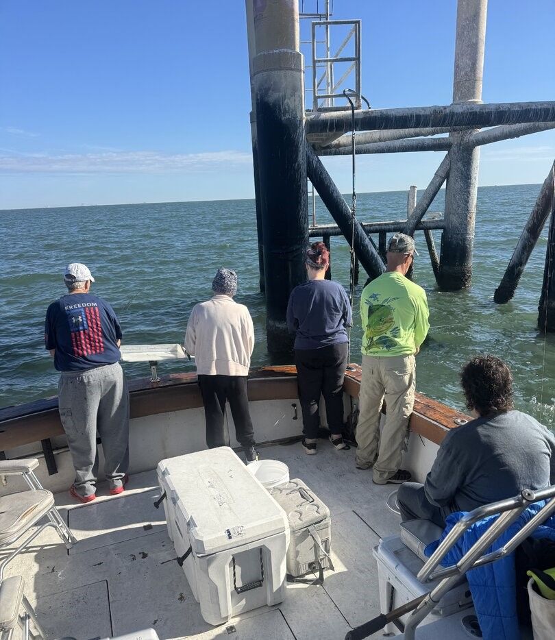 Fishing boat positioned near pier structure with anglers on deck over open water