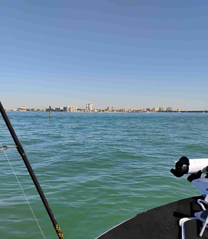 Fishing boat on open water with fishing rod and coastal buildings in background