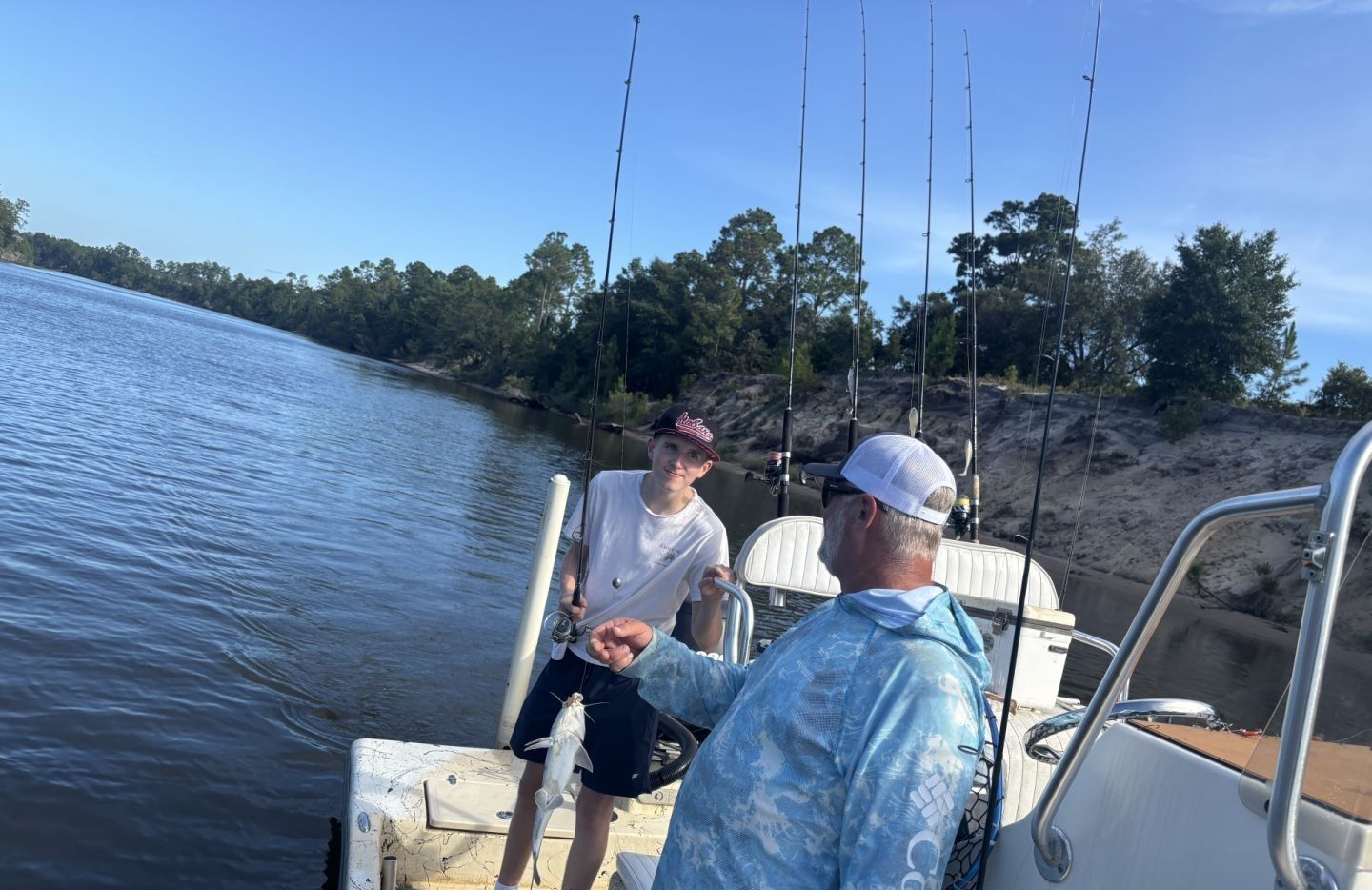 Fishing boat on calm water with multiple fishing rods set up along wooded shoreline