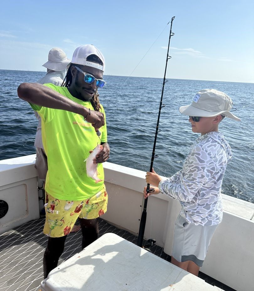 Fishing charter with crew member helping angler with caught fish on boat deck