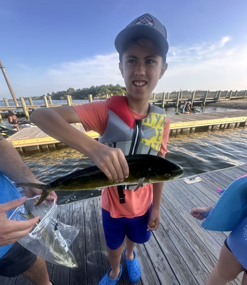 Freshly caught mahi mahi being displayed on fishing dock with wooden planks and water in background
