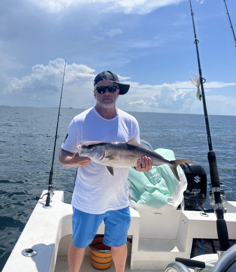 Angler holding caught Greater Amberjack on fishing boat at sea
