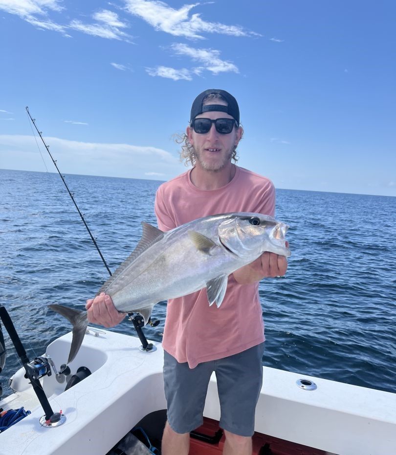 Angler holding caught Greater Amberjack fish on boat deck during ocean fishing trip