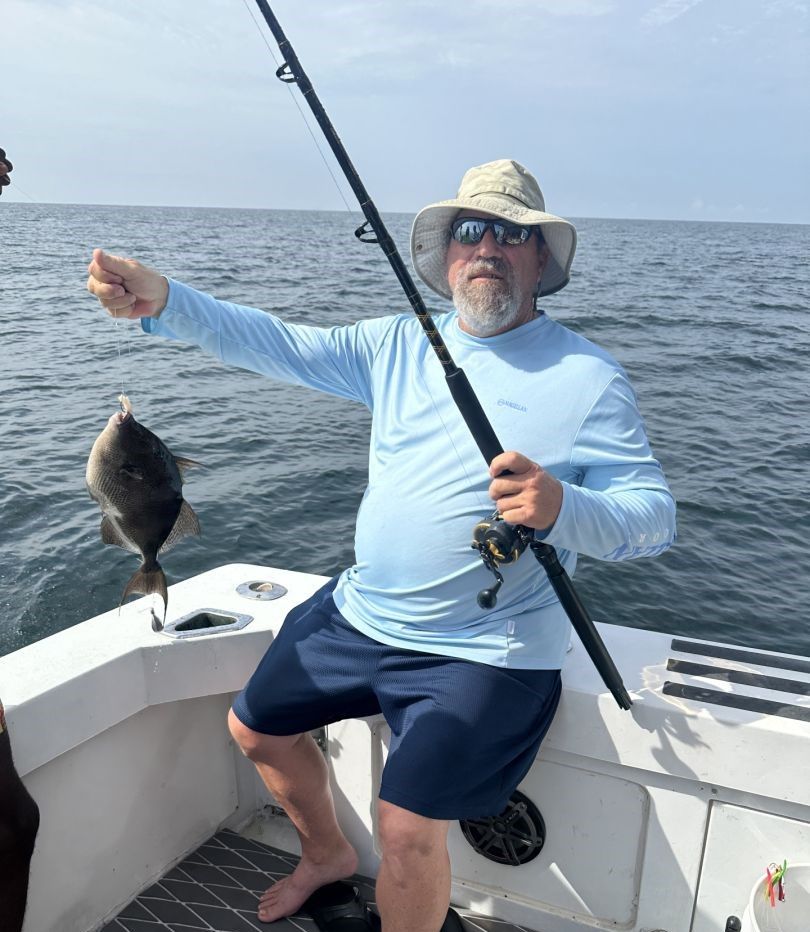 Angler holding caught grey triggerfish on fishing boat at sea