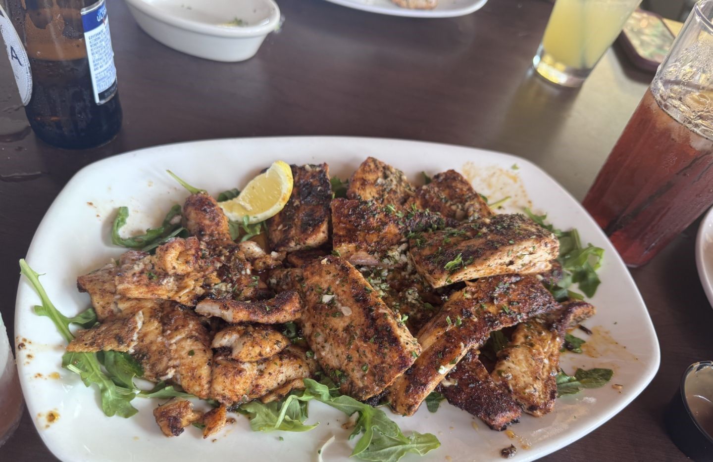 Grilled fish fillets seasoned with herbs served on a white platter with greens and lemon wedge