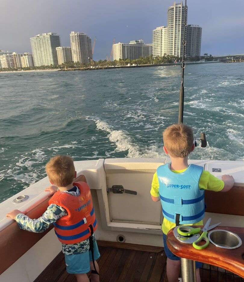 Two children in life jackets on fishing boat with city skyline in background